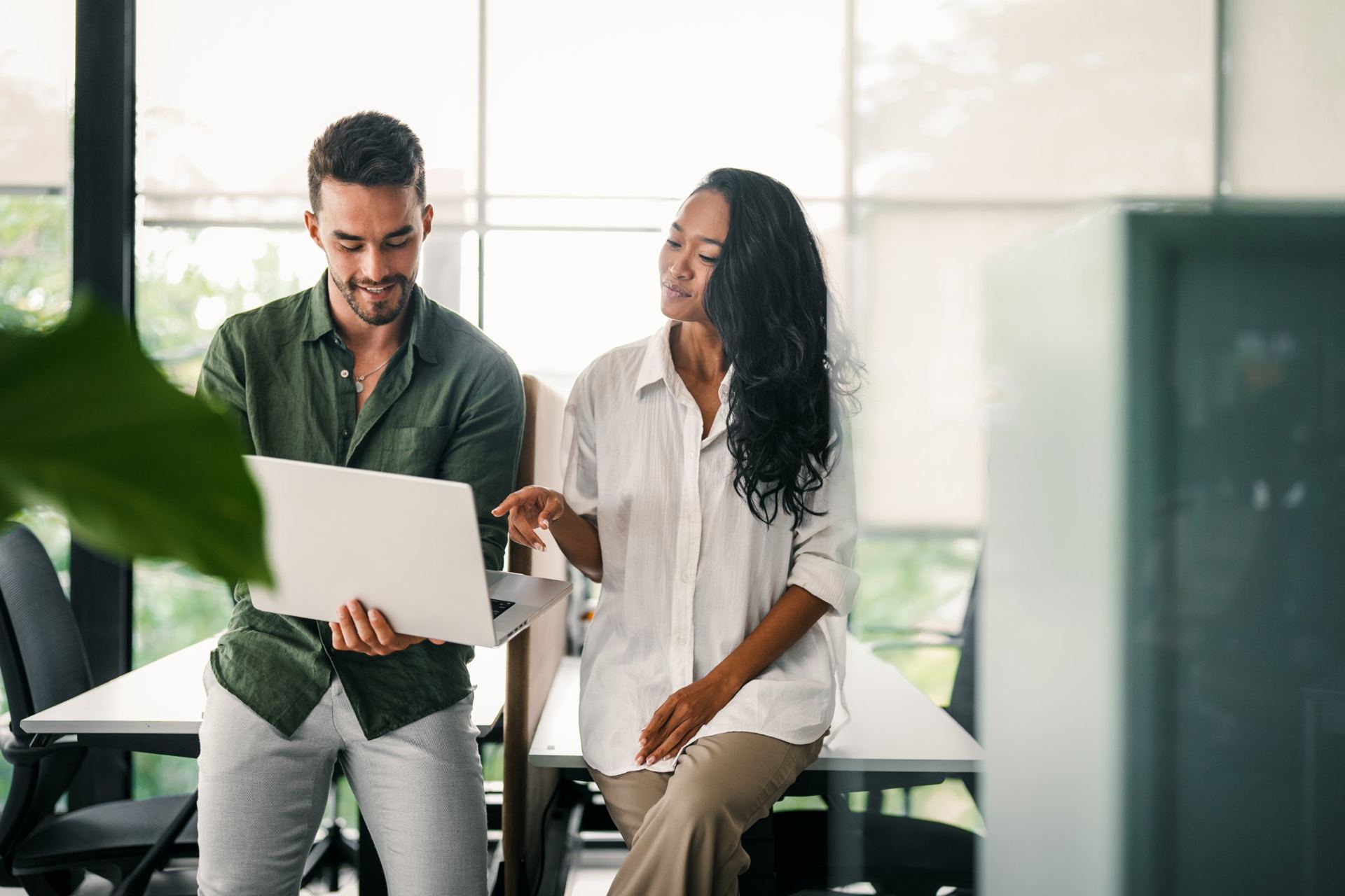 Two colleagues smiling over a laptop in a bright office
